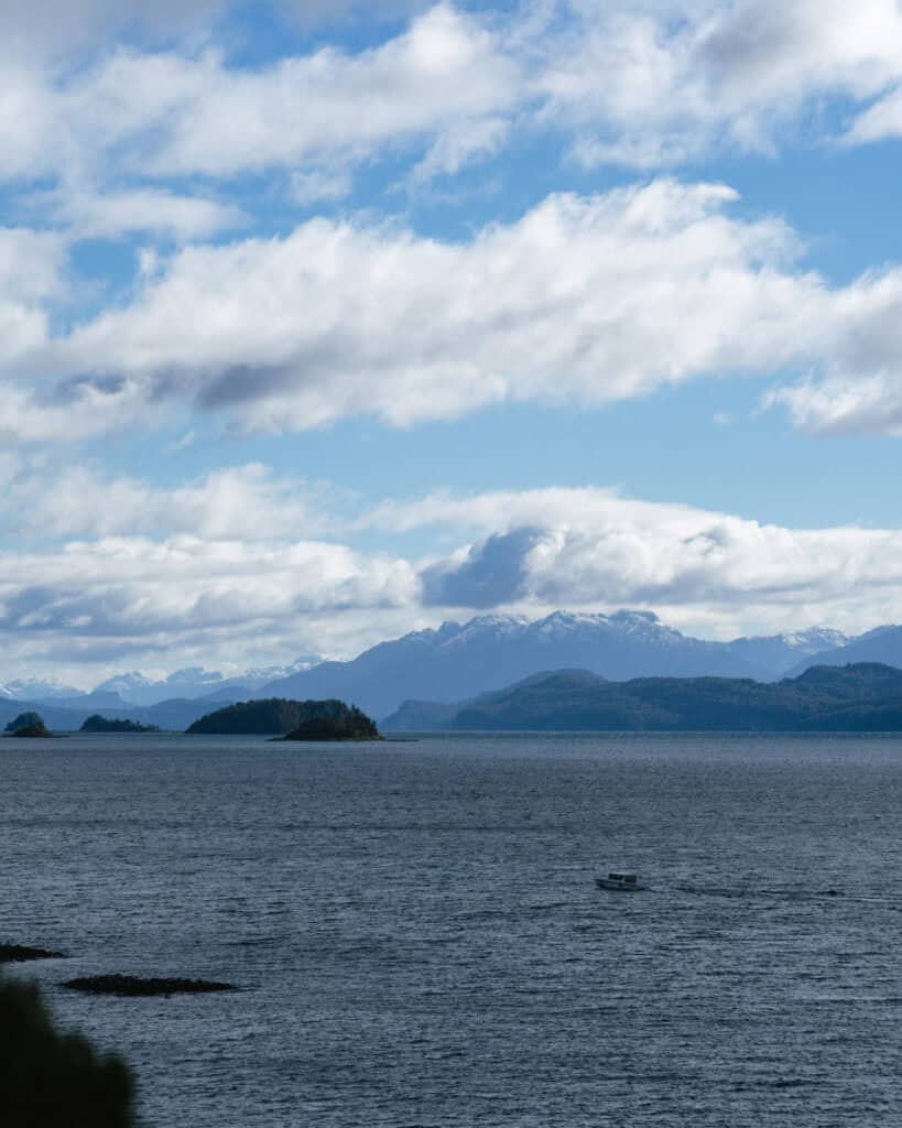 Cruce Andino: The Scenic Route From Chile to Argentina 35 Expansive view of Lago Nahuel Huapi with scattered small islands and a single boat crossing the water, backed by the snow-covered Andes under a dynamic blue and cloudy sky