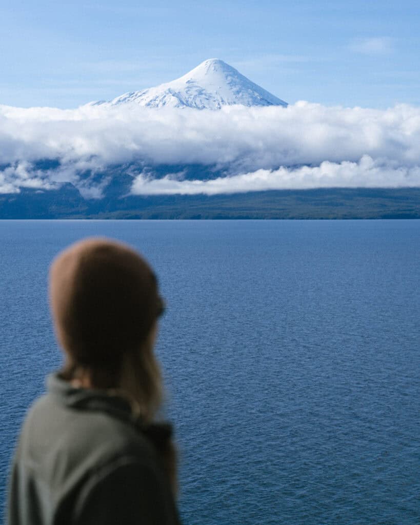 Cruce Andino: The Scenic Route From Chile to Argentina 3 With her back to the camera, Sally looks out over Lago Llanquihue toward Volcán Osorno, its snowy peak rising above a dense cloud line in Puerto Varas