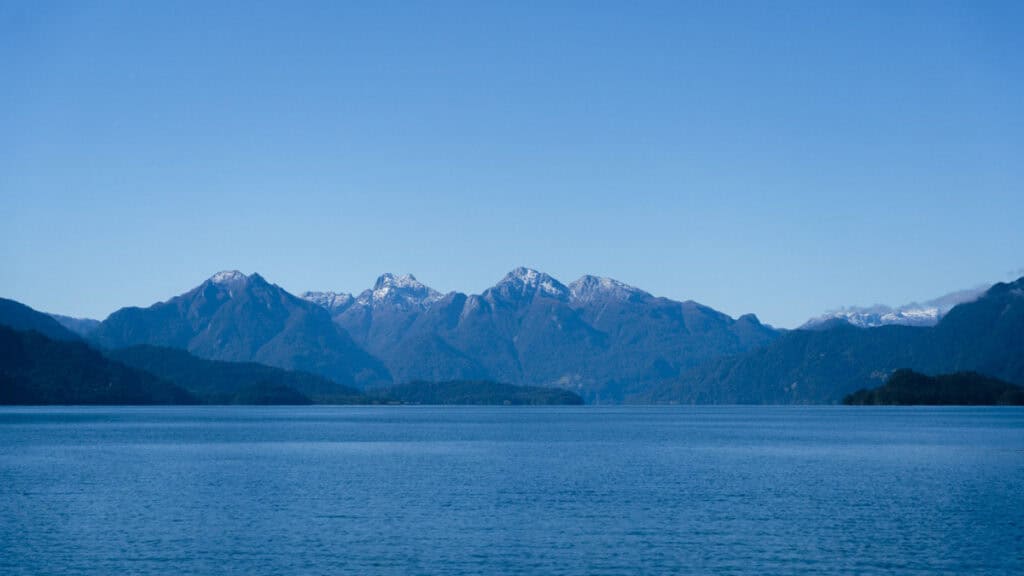 Cruce Andino: The Scenic Route From Chile to Argentina 6 Serene view of Lago Todos Los Santos near Puerto Varas, with calm blue waters and a backdrop of snow-topped Andean peaks under a bright sky