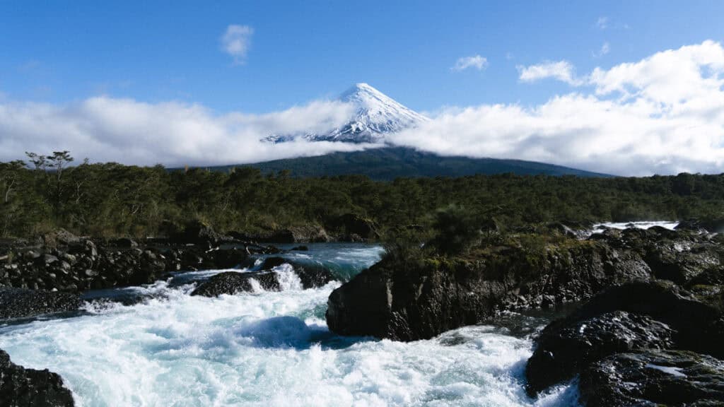 Cruce Andino: The Scenic Route From Chile to Argentina 8 Volcán Osorno rises dramatically behind a rushing river at Petrohue Falls, its snow-covered peak cutting through low clouds and framed by lush forest in southern Chile