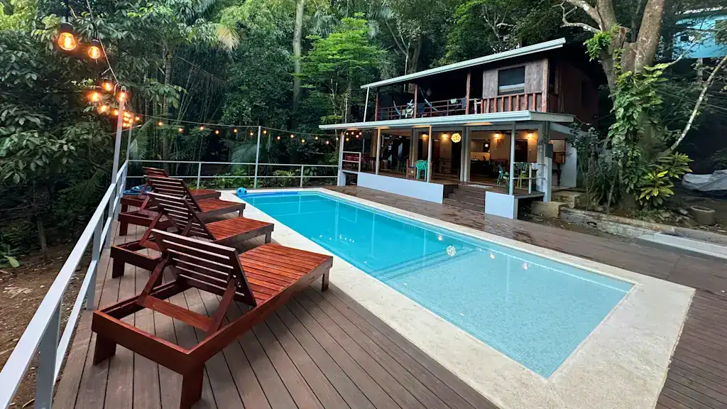 15 Best Things to Do in Montezuma Costa Rica 31 Luz en el Cielo Hostel in Montezuma Costa Rica, with a pool area lined by wooden loungers, surrounded by dense green jungle with the main hostel building in the background.