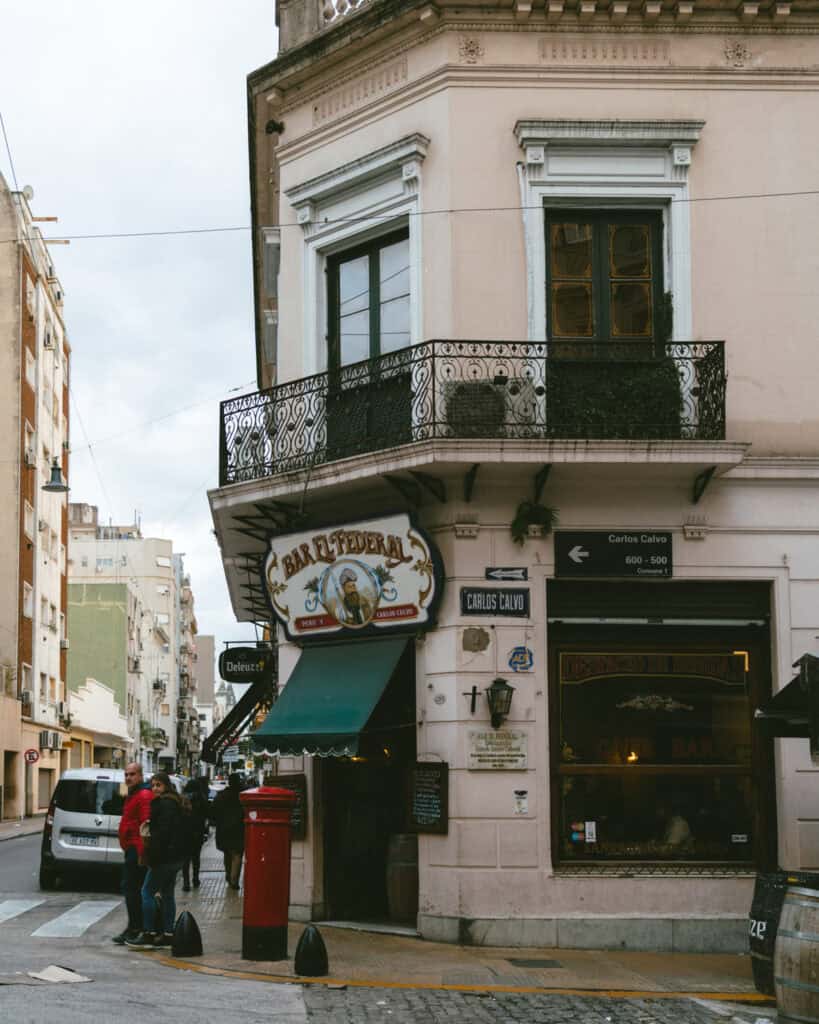 Buenos Aires Food Tour: Sherpa Food Tours in San Telmo 1 A wider street view of Bar El Federal at the intersection of Carlos Calvo and Perú streets, showing pedestrians, vintage architectural details, and the café’s large street-facing windows.