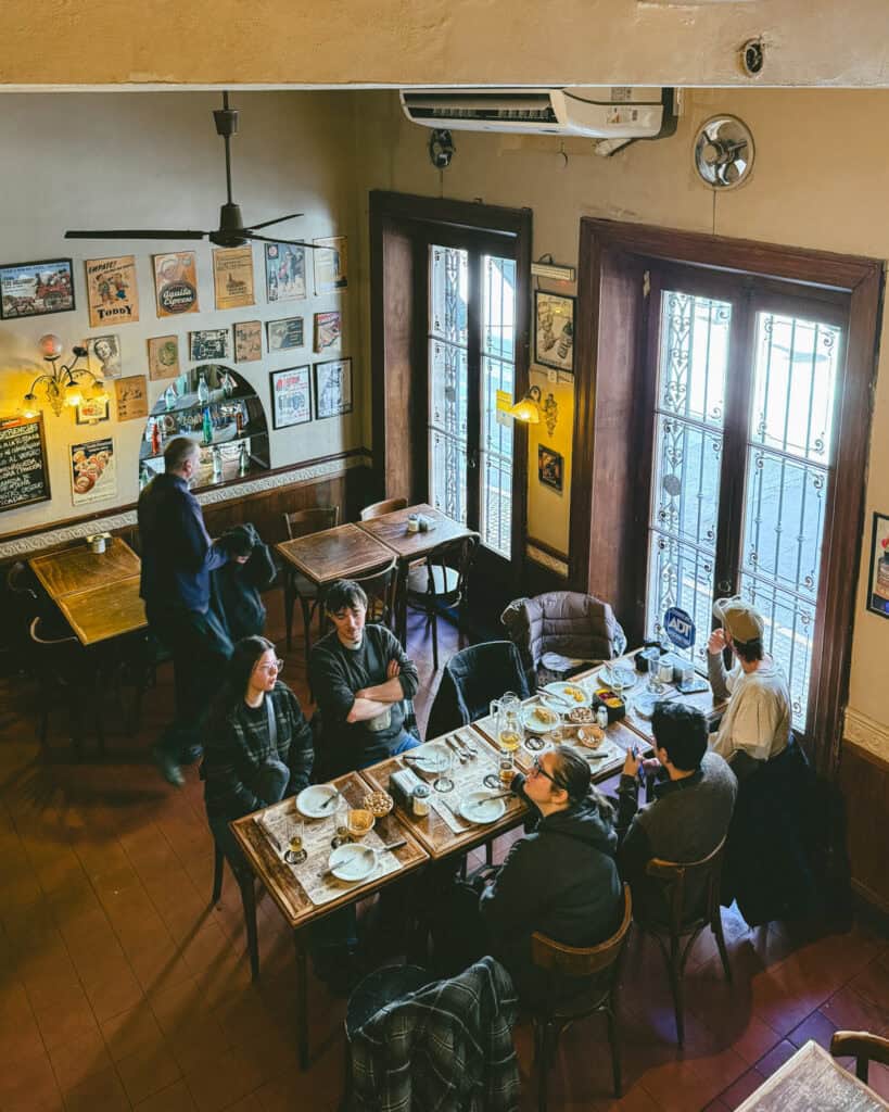 Buenos Aires Food Tour: Sherpa Food Tours in San Telmo 8 An overhead view of a table of diners finishing their meal inside Bar El Federal in Buenos Aires. The cozy interior is decorated with vintage posters and dark wooden furniture.