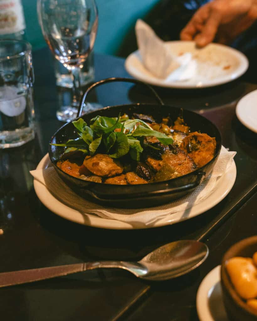 Buenos Aires Food Tour: Sherpa Food Tours in San Telmo 13 A cast iron dish filled with sautéed vegetables including squash, zucchini, and potatoes, garnished with fresh greens, served on a white plate in a Buenos Aires restaurant setting.
