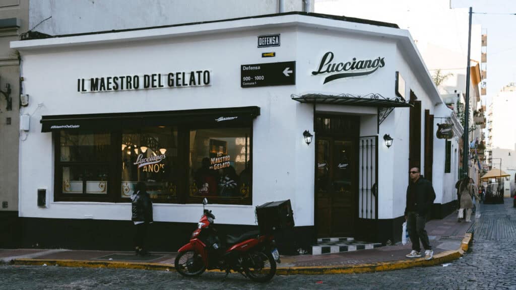 Buenos Aires Food Tour: Sherpa Food Tours in San Telmo 4 The white corner façade of Lucciano’s gelateria in San Telmo, Buenos Aires, with signs reading “Il Maestro del Gelato” and “Lucciano’s,” and a red delivery motorcycle parked outside.
