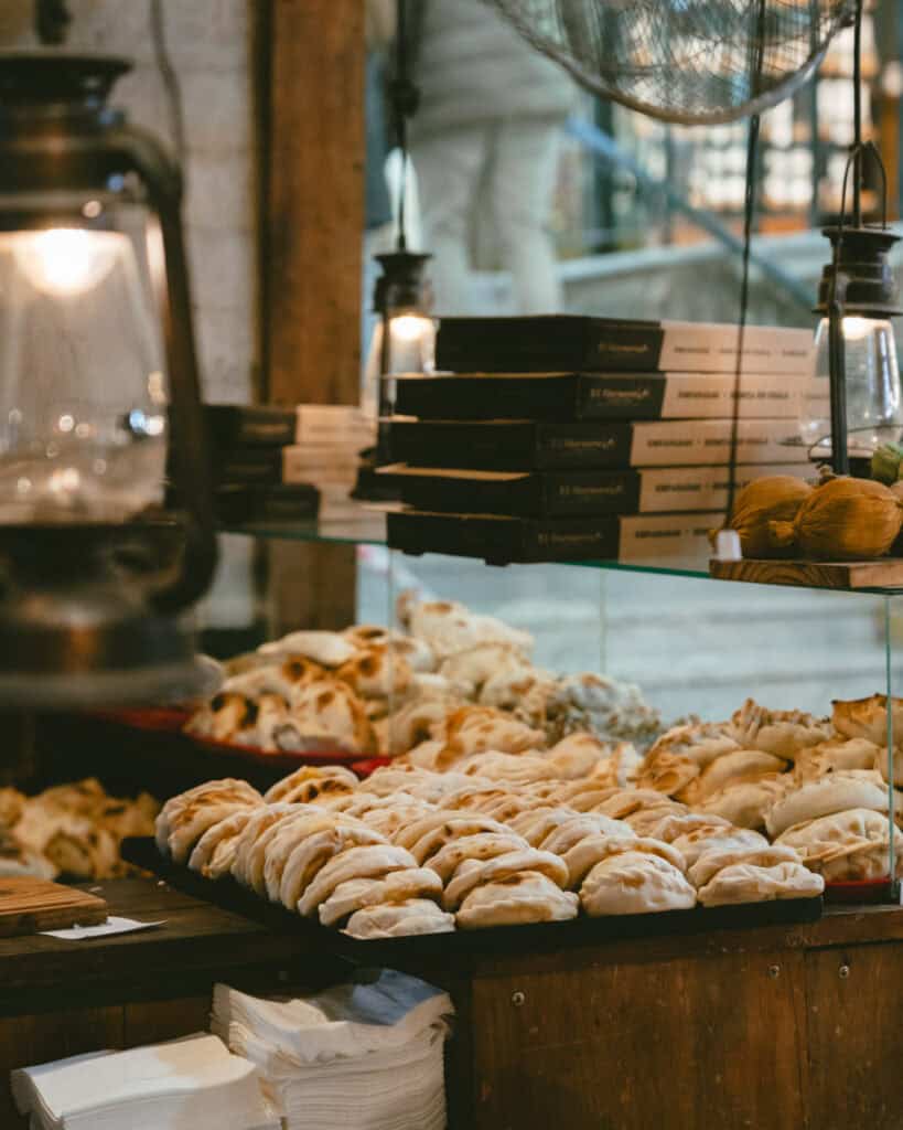 Buenos Aires Food Tour: Sherpa Food Tours in San Telmo 3 A rustic market stall lined with lanterns and wooden trays piled high with freshly baked empanadas in varying styles, from braided to crimped, behind a glass display.