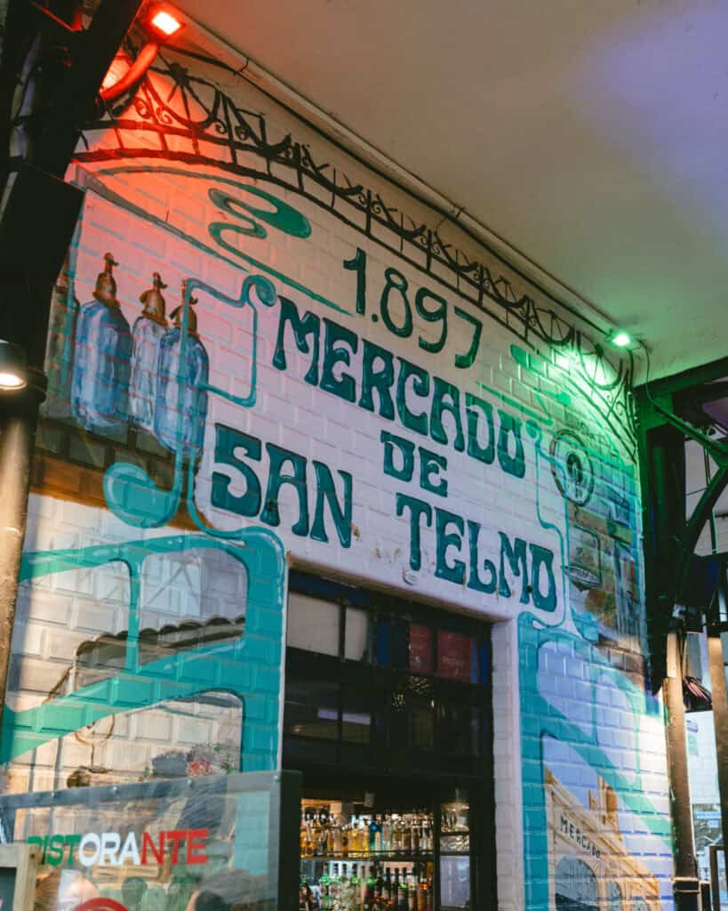 Buenos Aires Food Tour: Sherpa Food Tours in San Telmo 18 Colorful mural entrance to Mercado de San Telmo painted on white tile, featuring soda siphon bottles and the year 1897 in bold above the market name.