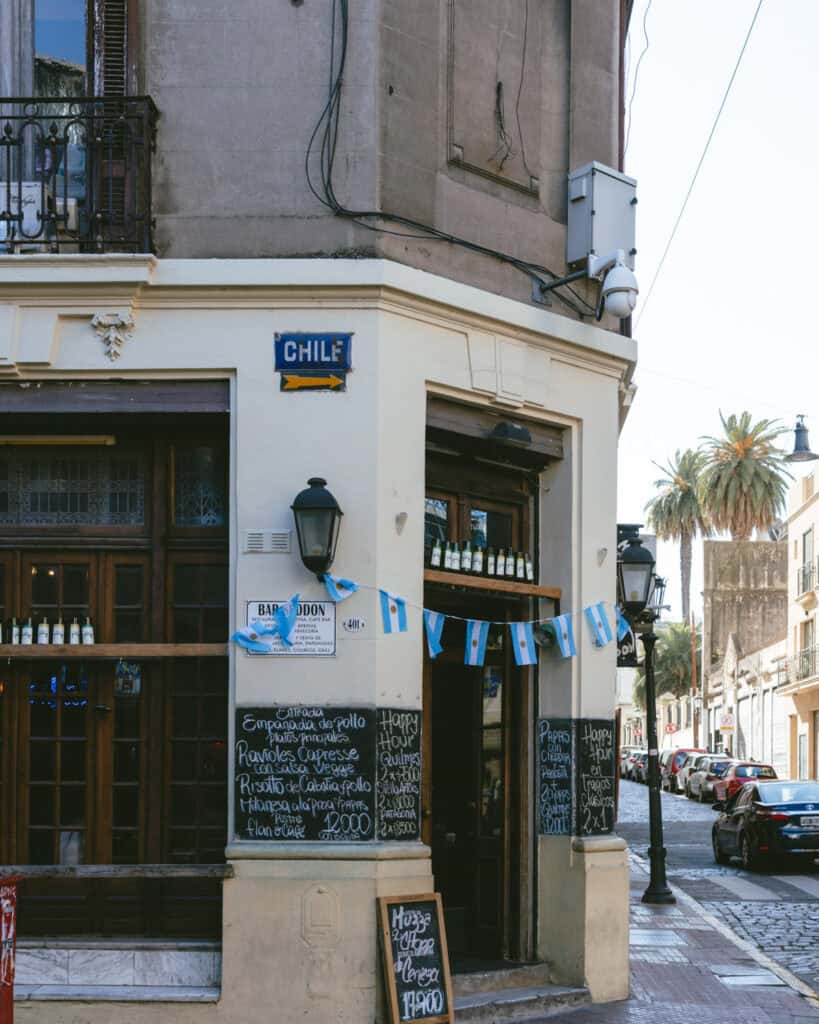 Buenos Aires Food Tour: Sherpa Food Tours in San Telmo 21 Corner cafe in Buenos Aires decorated with small Argentine flags and chalkboard menus listing empanadas, ravioles caprese, and happy hour specials, located at the intersection of Bar Bolson and Chile Street.