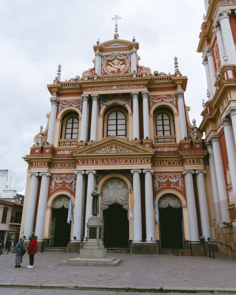 7 - 10 Day Salta Road Trip: The Best of Northwest Argentina 8 Iglesia San Francisco in Salta featuring a richly decorated red, gold, and white neoclassical facade with Corinthian columns and religious statues, with a few people standing at the base.