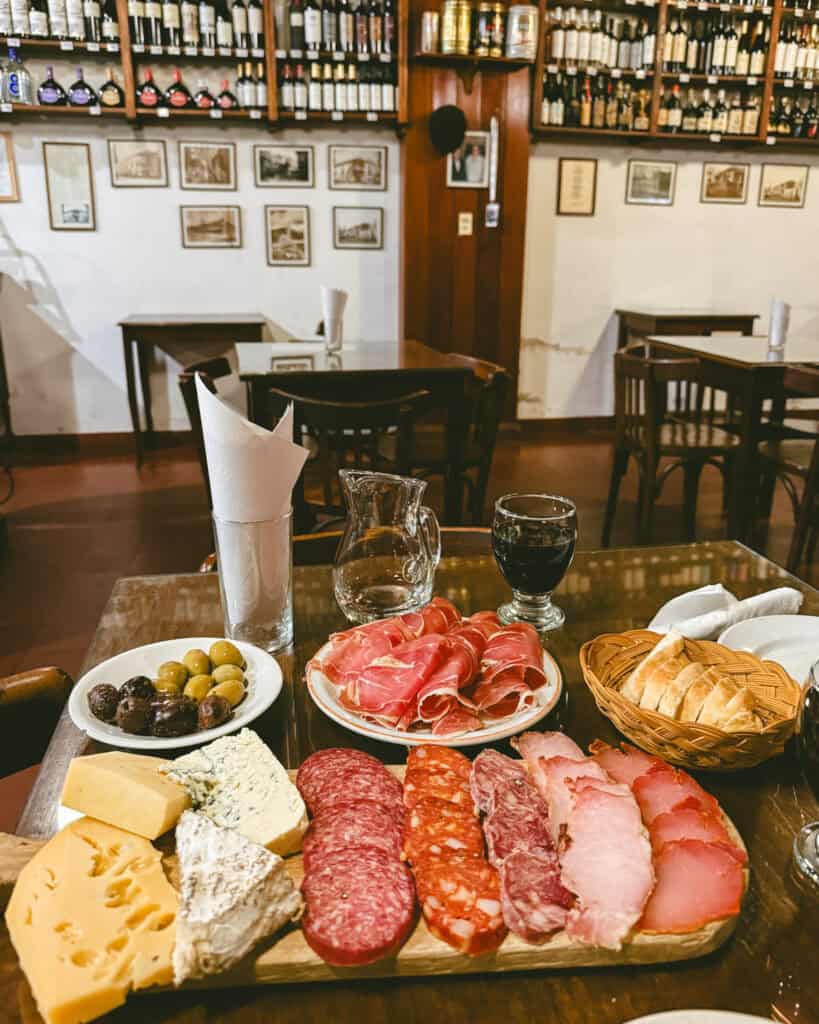 7 - 10 Day Salta Road Trip: The Best of Northwest Argentina 15 Wooden table set with a traditional Argentine picada platter of assorted cheeses, cured meats, olives, bread, and glasses of red wine in Casa Moderna’s dining area.