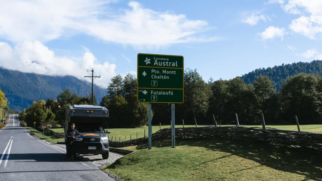Puyuhuapi, Chile Travel Guide: Fjords and Hanging Glaciers 7 Roadside view of a green sign for Carretera Austral in Chaitén, with directions to Pto. Montt, Chaitén, and Futaleufú, with a camper truck and Brayden nearby.