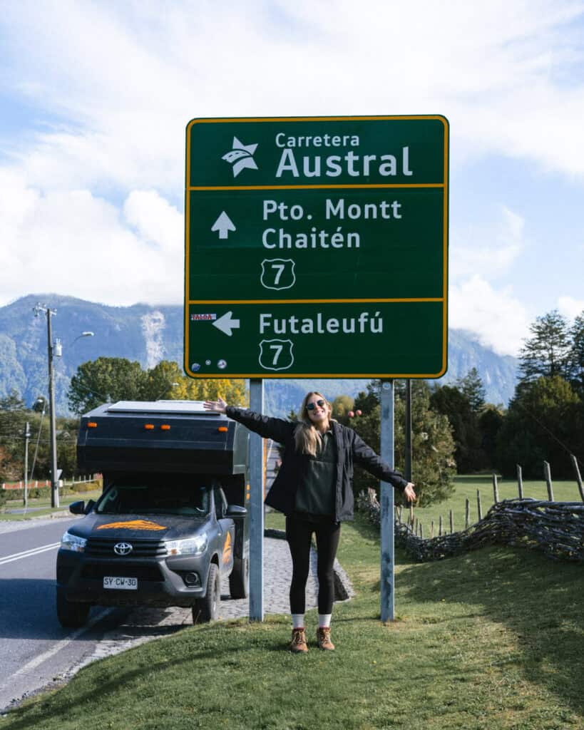 The Carretera Austral, Chile: Everything You Need to Know 5 Sally poses with arms outstretched in front of a Carretera Austral road sign in Chaitén, showing directions to Pto. Montt, Chaitén, and Futaleufú, with a camper truck behind her.