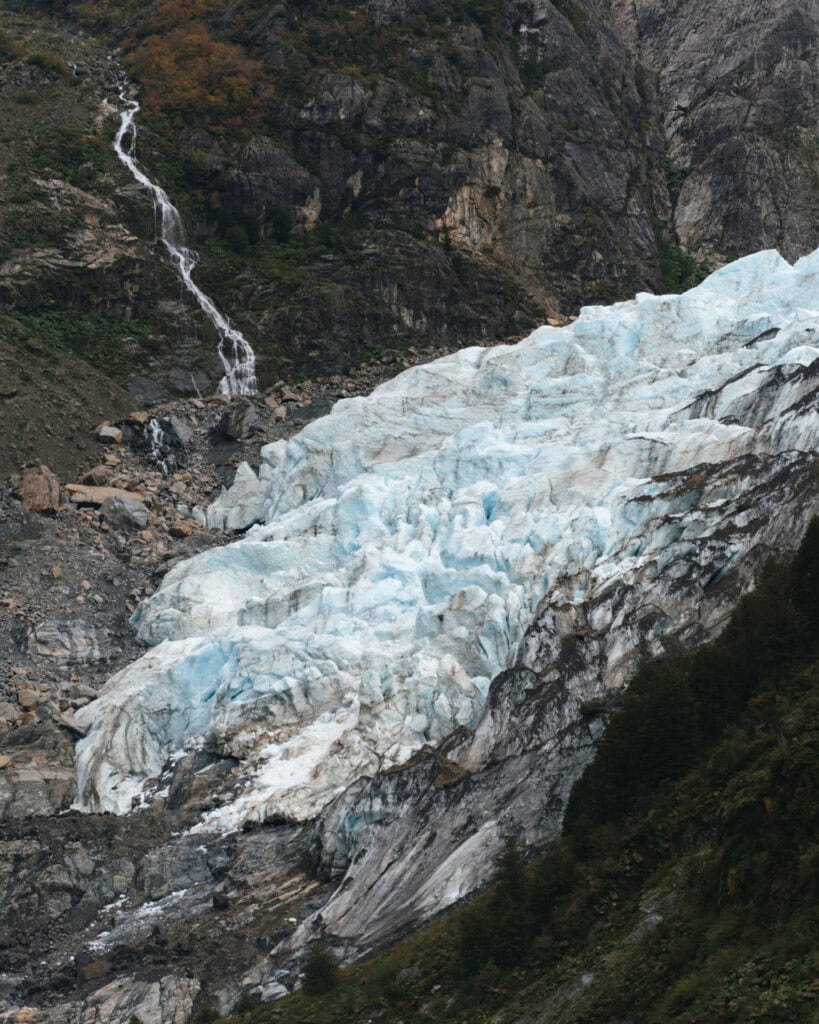 Chaiten, Chile Travel Guide: A Town That Nearly Disappeared 26 Bottom edge of a glacier in Chaitén where ice meets rocky ground, with a nearby cascading waterfall running down a steep cliff.