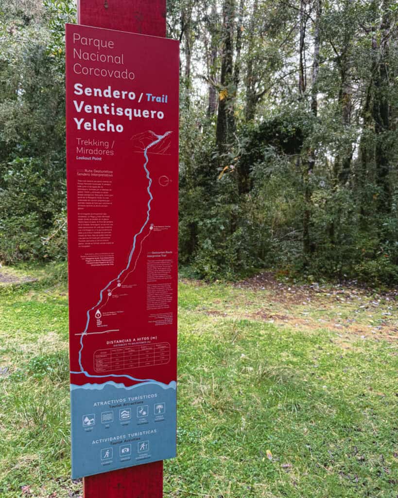 Ventisquero Yelcho Hike Guide: Corcovado National Park, Chile 9 Red and blue trailhead sign for Sendero Ventisquero Yelcho in Parque Nacional Corcovado, Chaitén, featuring a map, distance markers, and tourist activity icons.