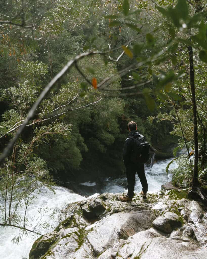 Chaiten, Chile Travel Guide: A Town That Nearly Disappeared 12 Brayden stands on a wet rocky ledge above a fast-moving river, gazing into the misty forest.