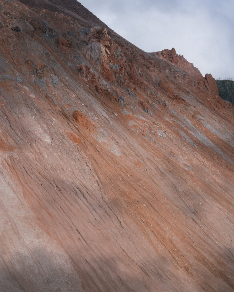 How to Visit the Pumalin National Park in Patagonia, Chile 32 Textured close-up of rocky, red-orange volcanic debris on the Chaitén slope with patches of exposed rock and soil layers.