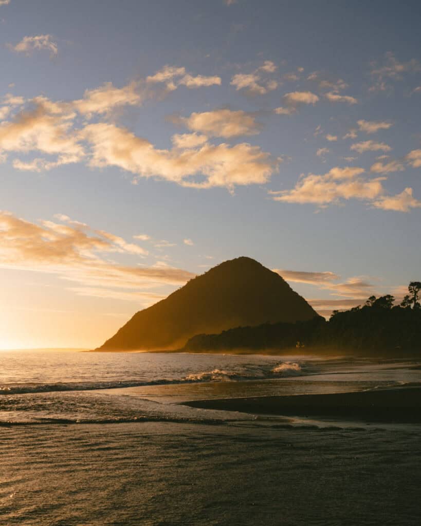 Chaiten, Chile Travel Guide: A Town That Nearly Disappeared 2 Volcano near the coast glows at sunset, casting dramatic shadows over the ocean and shoreline, with golden clouds overhead.
