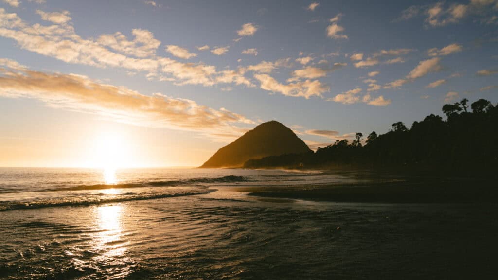 Chaiten, Chile Travel Guide: A Town That Nearly Disappeared 23 Sunset over the Pacific with a cone-shaped coastal volcano in the distance, warm golden light reflecting off the waves and clouds.