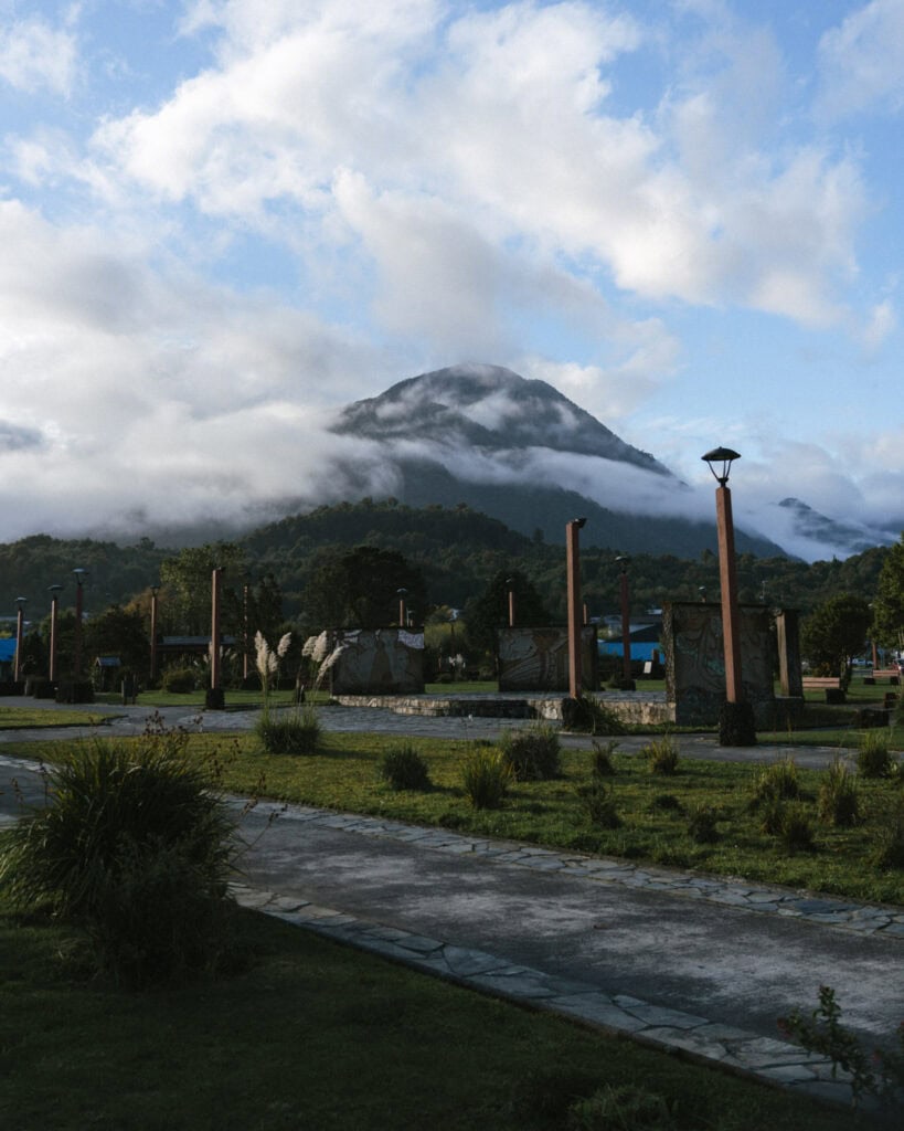 Chaiten, Chile Travel Guide: A Town That Nearly Disappeared 20 Chaitén Volcano shrouded in mist and low clouds behind a landscaped park with lamp posts, murals, and walking paths in town.