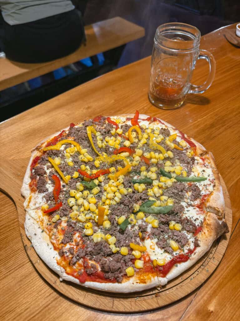 Chaiten, Chile Travel Guide: A Town That Nearly Disappeared 29 Close-up of a pizza topped with ground meat, corn, and bell peppers on a wooden table, with a glass mug and steam rising in the background.