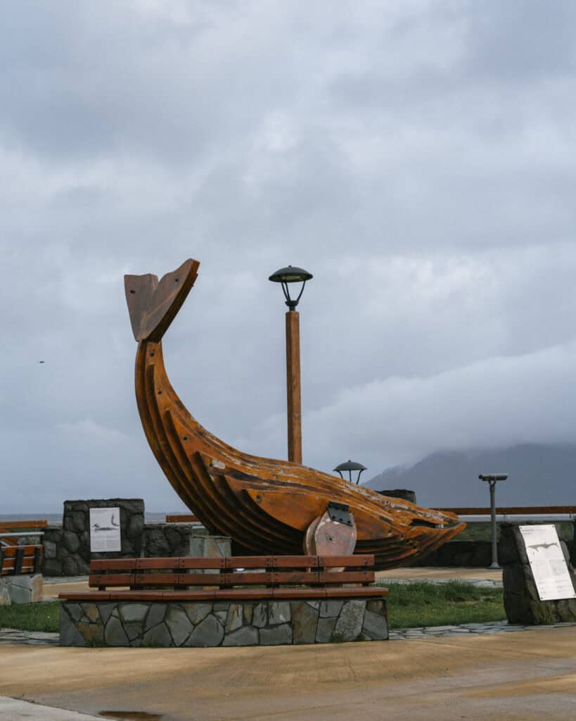 Chaiten, Chile Travel Guide: A Town That Nearly Disappeared 21 Large rust-colored wooden whale tail sculpture displayed at Chaitén’s waterfront promenade, surrounded by benches and interpretive signs.