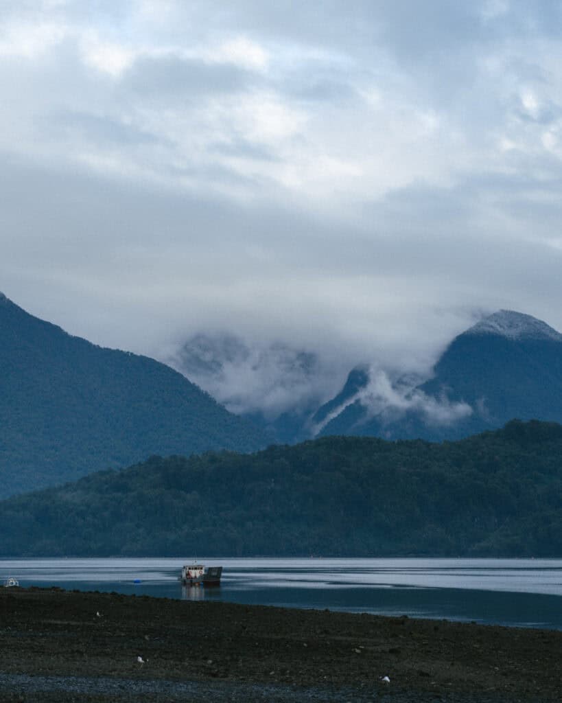 Hornopiren, Chile Travel Guide: Termas, Alerces & Fjords 3 Fishing boat anchored in the bay of Hornopirén, Chile, with dramatic mist covering the surrounding mountain peaks and dense green forest.