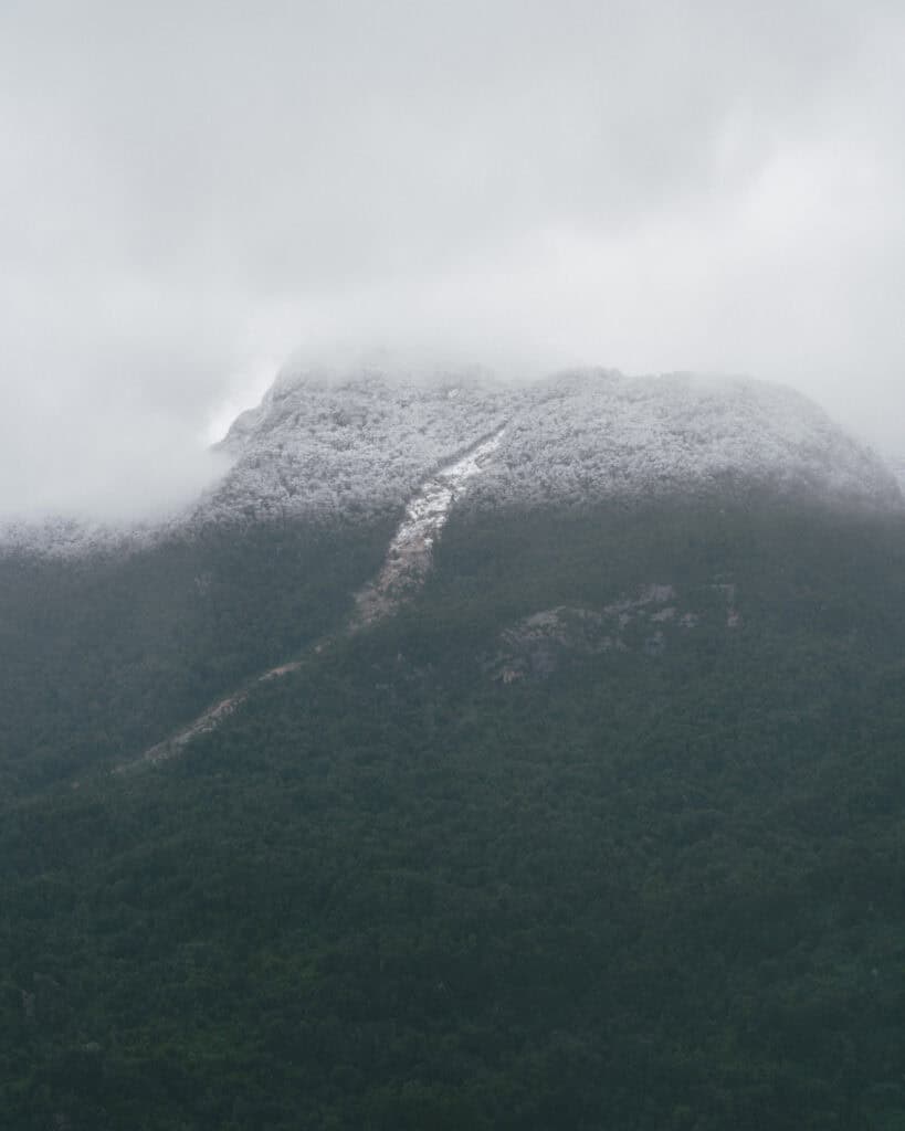 Hornopiren, Chile Travel Guide: Termas, Alerces & Fjords 1 Snow-dusted mountain peak in Hornopirén, Chile, partly hidden by heavy clouds, rising above dense green forest.