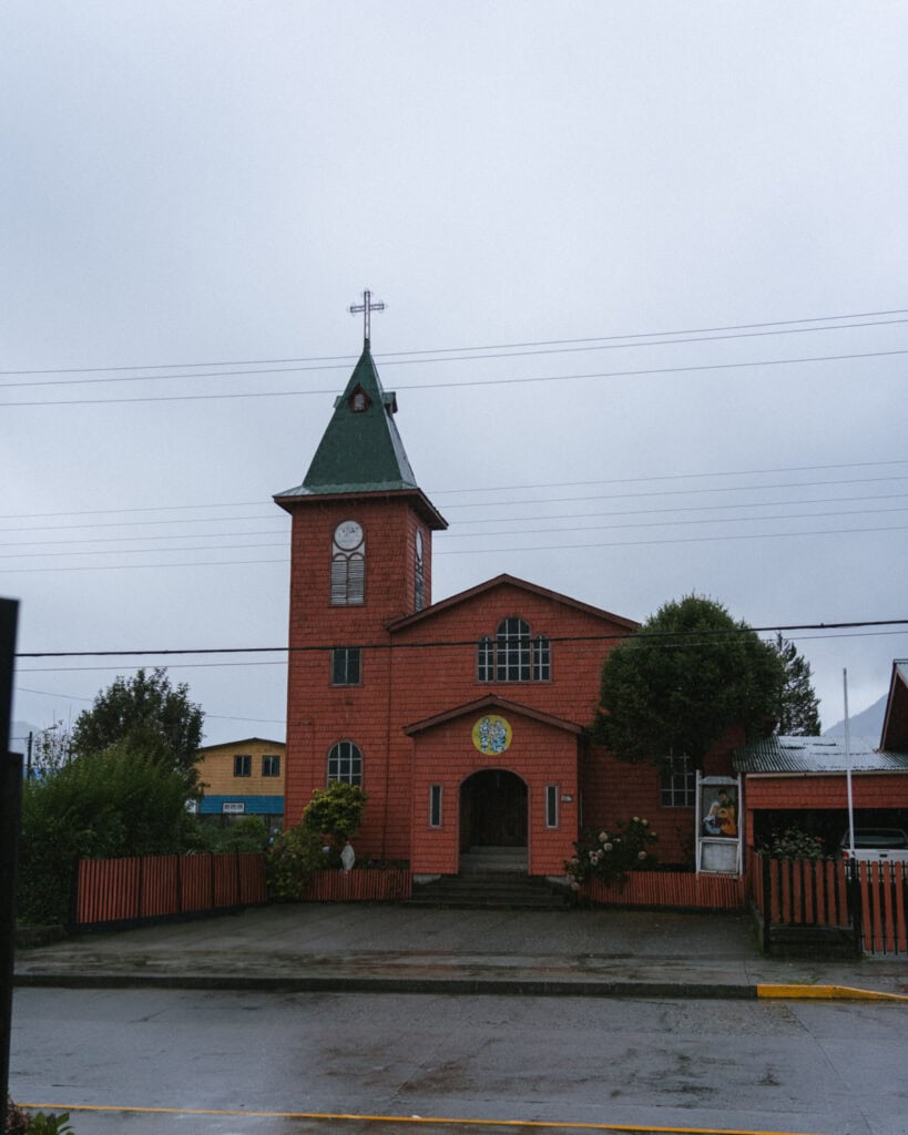 Hornopiren, Chile Travel Guide: Termas, Alerces & Fjords 21 Red wooden church with a green roof and cross-topped tower on a rainy day in Hornopirén, Chile.