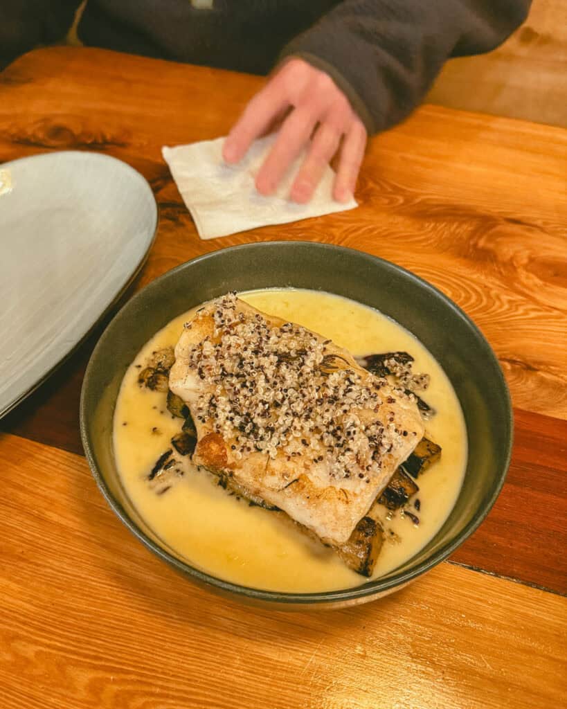 Hornopiren, Chile Travel Guide: Termas, Alerces & Fjords 32 Bowl of fish fillet topped with quinoa served in a creamy yellow sauce at a restaurant table in Hornopirén, Chile.