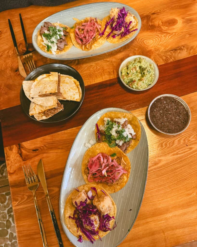 Hornopiren, Chile Travel Guide: Termas, Alerces & Fjords 30 Plates of tacos, quesadillas, guacamole, and black beans on a wooden table at a restaurant in Hornopirén, Chile.