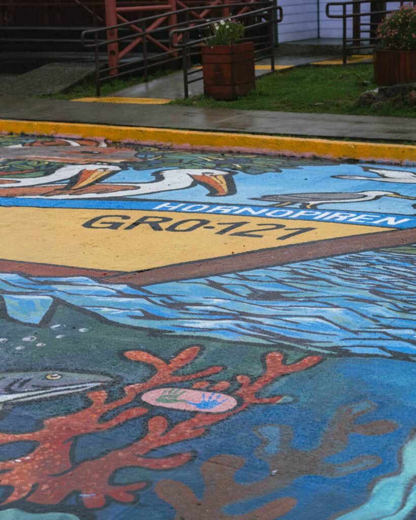 Hornopiren, Chile Travel Guide: Termas, Alerces & Fjords 22 Colorful street mural on the pavement in Hornopirén, Chile, depicting fish, coral, and seabirds with the word “Hornopirén.”