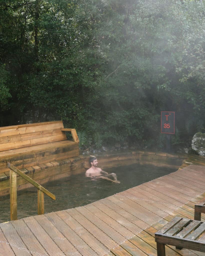 Hornopiren, Chile Travel Guide: Termas, Alerces & Fjords 16 Brayden relaxing in a steaming hot spring pool with a temperature sign of 35 degrees Celsius at Hornopirén, Chile.