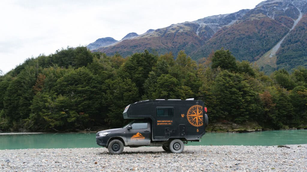 Puerto Rio Tranquilo, Chile Travel Guide: Marble & Ice 13 Our Camper Travel Chile 4x4 camper parked on a rocky river bank at Rio Murta, with a bright turquoise river behind and forest-clad mountains rising up from the river.