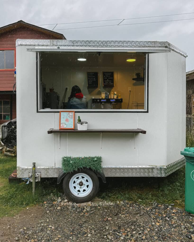 Puyuhuapi, Chile Travel Guide: Fjords and Hanging Glaciers 22 Small white coffee cart with a serving window, a person inside preparing drinks, and a menu on display, set in Puyuhuapi, Chile.