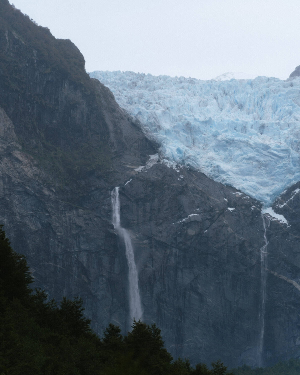 Our Epic 3-Week Carretera Austral Road Trip Itinerary 52 Close-up of the Hanging Glacier with a tall waterfall plunging from the ice field down rocky cliffs in Parque Nacional Queulat, Chile.