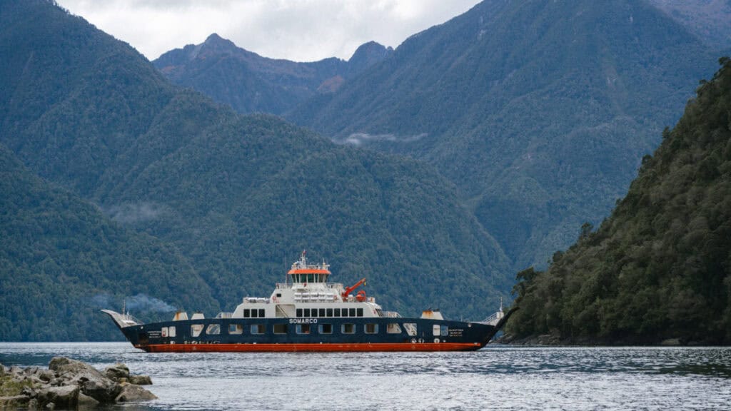 Carretera Austral Ferries Guide: Mandatory + Optional Routes 1 One of the Carretera Austral ferries, the barge from Hornopiren - Caleta Gonzalo with SOMARCO, sitting in a scenic fjord surrounded by forest-clad mountains.