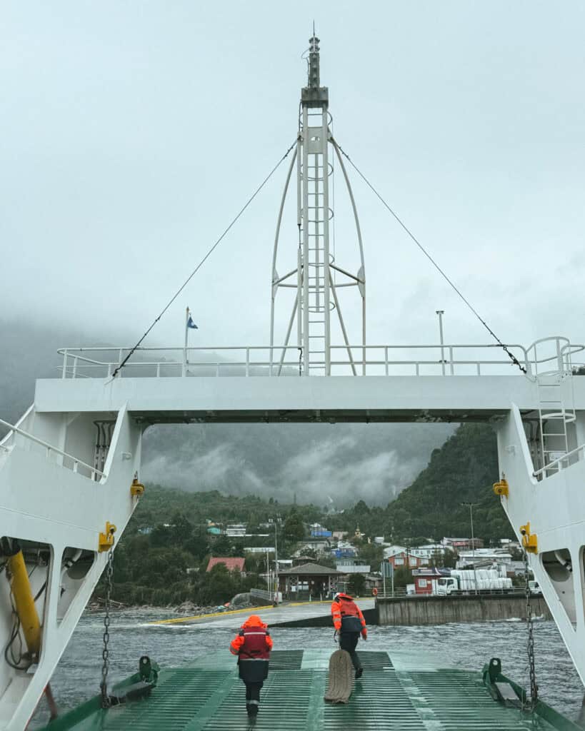 Carretera Austral Ferries Guide: Mandatory + Optional Routes 4 Two workers in high vis jackets are on one of the Carretera Austral ferries from Caleta La Arena - Caleta Puelche on a grey, foogy day with cloud and mist hanging on the mountains.