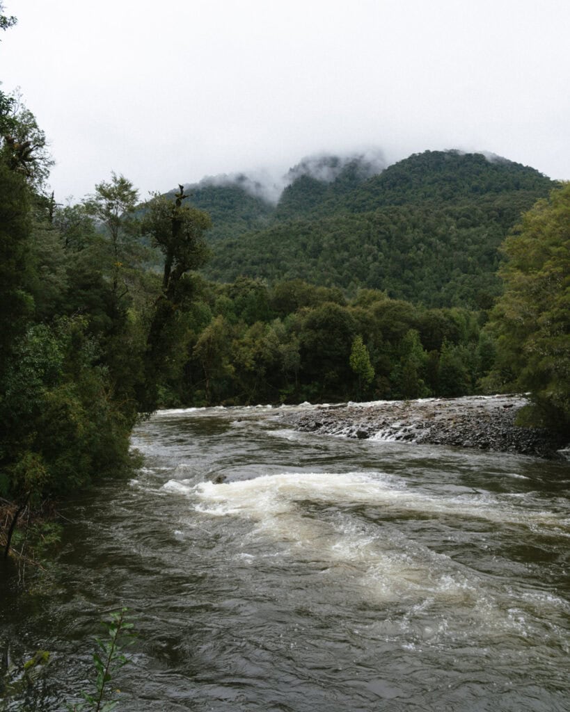 How to Visit the Alerce Andino National Park, Chile 15 The Rio Lenca in Alerce Andino National Park, against a moody sky with cloud and fog hanging over the forested hills.