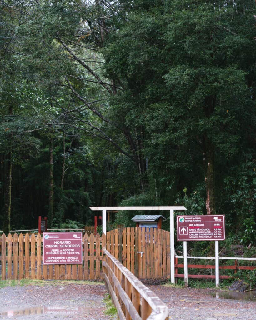 How to Visit the Alerce Andino National Park, Chile 6 The entry to Alerce Andino National Park, with multiple wooden signs about the park's access hours and trail distances.