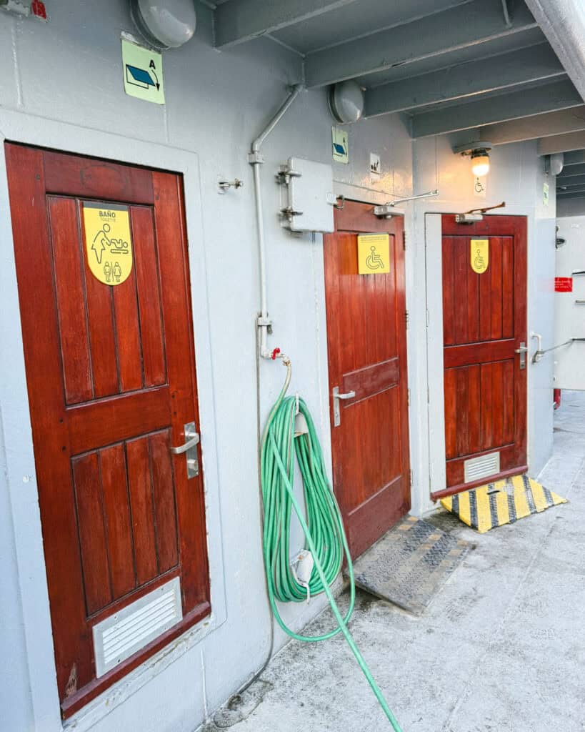 TABSA Ferry: Sailing from Puerto Natales to Puerto Yungay 24 Exterior view of three red restroom doors aboard the Tabsa Ferry in Chile, labeled with yellow signage for changing tables and wheelchair accessibility, with a green hose coiled nearby and ramps for access.