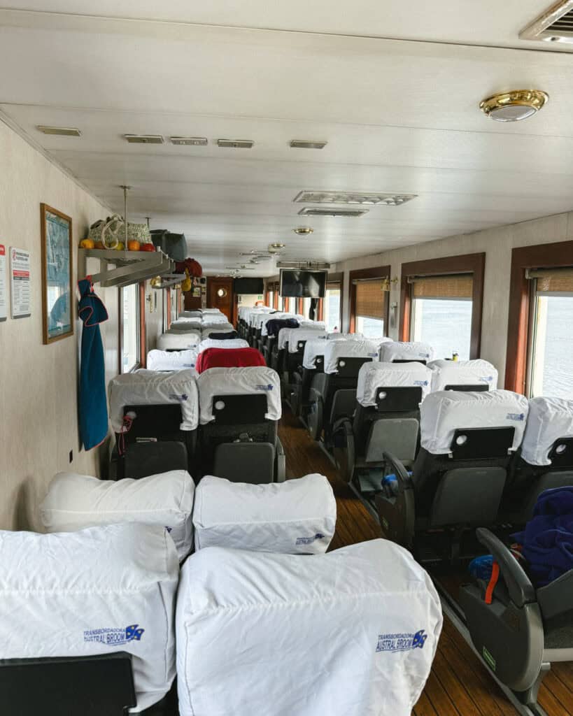 TABSA Ferry: Sailing from Puerto Natales to Puerto Yungay 19 Another angle of the Tabsa Ferry’s passenger seating area, featuring white headrest covers and wide windows with views of the water; Brayden adjusts his bag in the aisle.