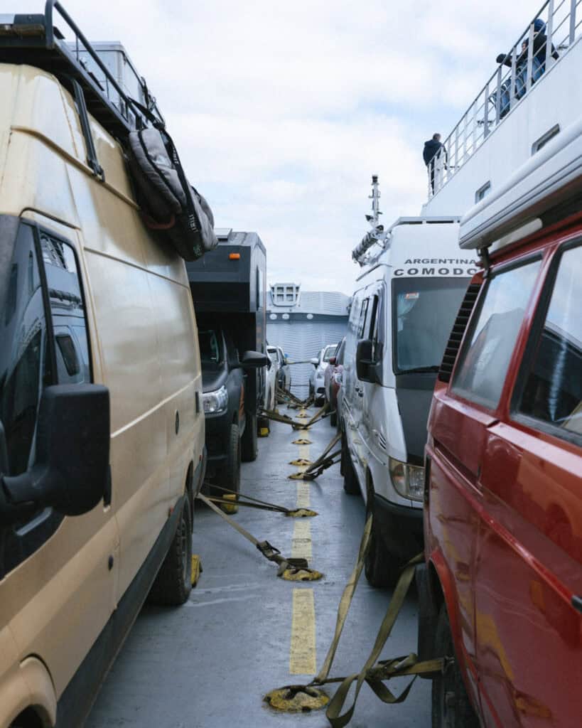 TABSA Ferry: Sailing from Puerto Natales to Puerto Yungay 18 Tight row of camper vans and utility vehicles secured with yellow straps on the car deck of the Tabsa Ferry in Chile, with Brayden visible on the upper deck railing.