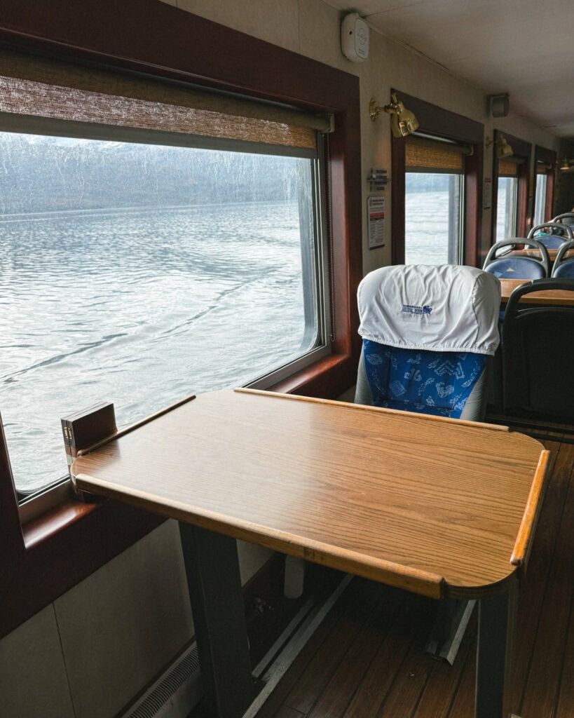 TABSA Ferry: Sailing from Puerto Natales to Puerto Yungay 31 Wooden table and blue seat beside a large window aboard the Tabsa Ferry in Chile, offering a peaceful view of the Patagonian fjords as the ferry glides through the water.