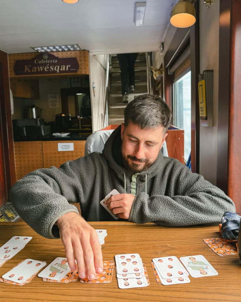 TABSA Ferry: Sailing from Puerto Natales to Puerto Yungay 34 Brayden plays a game of cards on a wooden table inside the Tabsa Ferry’s Cafetería Kawésqar, concentrating as he places a card down with rows of illustrated playing cards spread out in front of him.