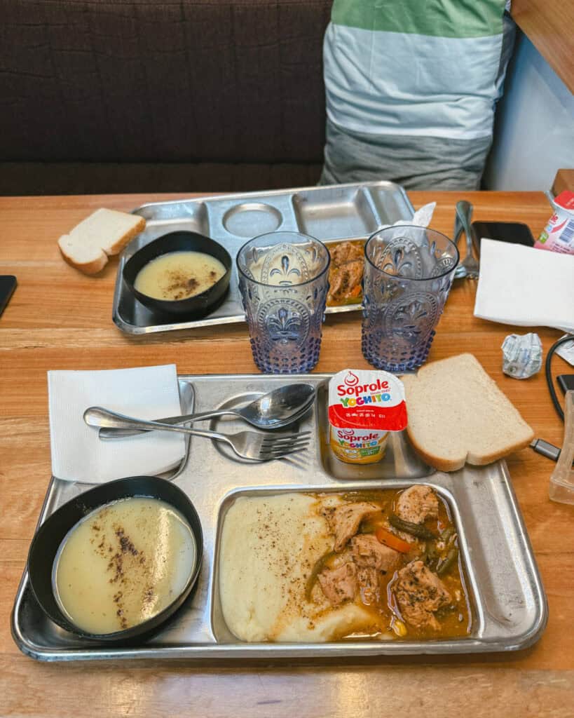TABSA Ferry: Sailing from Puerto Natales to Puerto Yungay 32 Hearty meal of mashed potatoes with stewed chicken, a slice of bread, yogurt, and soup served on metal trays aboard the Tabsa Ferry in Chile, with ornate plastic cups set on the table.