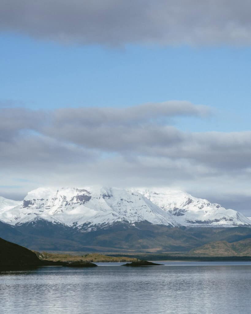TABSA Ferry: Sailing from Puerto Natales to Puerto Yungay 3 Majestic snow-covered peaks of the Torres del Paine mountain range towering above the Patagonian steppe, with calm waters in the foreground, viewed from the ferry.