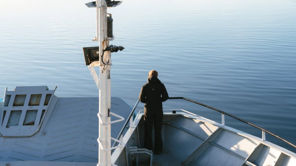 TABSA Ferry: Sailing from Puerto Natales to Puerto Yungay 4 Brayden in a beanie and black jacket stands alone at the bow of the Tabsa Ferry, gazing over the still, glassy waters of the Patagonian fjords during golden hour.