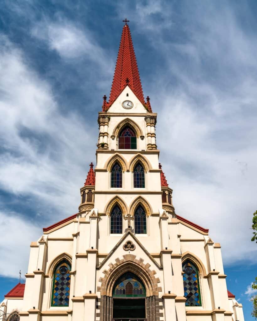 Costa Rica Travel Guide: Planning The Perfect Pura Vida Trip 21 La Merced Church in San Jose, Costa Rica with a cream exterior and deep red roof with pointy spire.