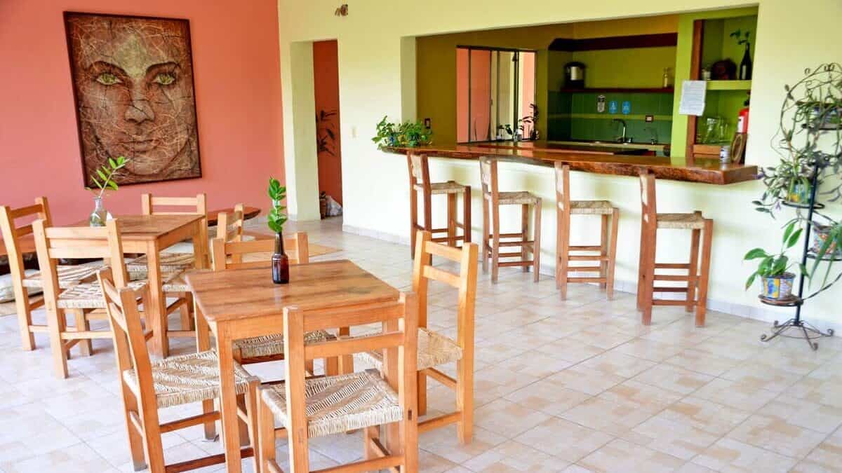 San Pancho Mexico Travel Guide: Tropical Bliss in Nayarit 10 A communal dining and chill area at Hostal San Pancho Nayarit Mexico, with a dining table and chairs with stools against a breakfast bar in the kitchen behind.