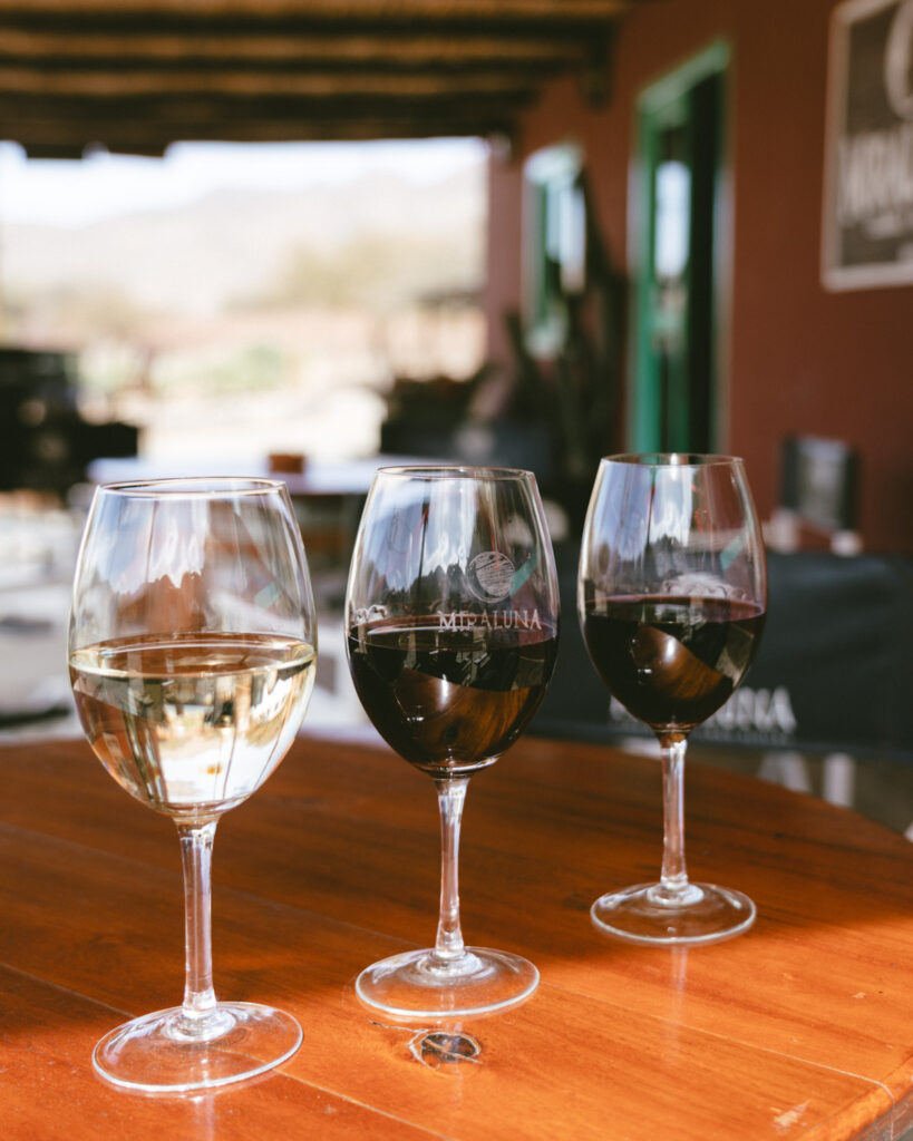 7 - 10 Day Salta Road Trip: The Best of Northwest Argentina 47 Three wine glasses—one white and two red—sit on a polished wooden table at Miraluna winery in Cachi, with the branded logo visible on the center glass.